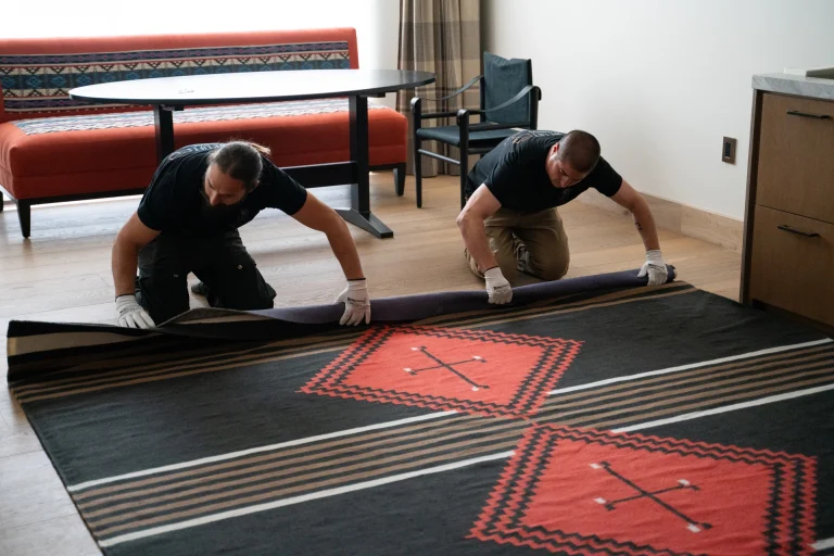 Two delivery men placing an oversized rug in a room