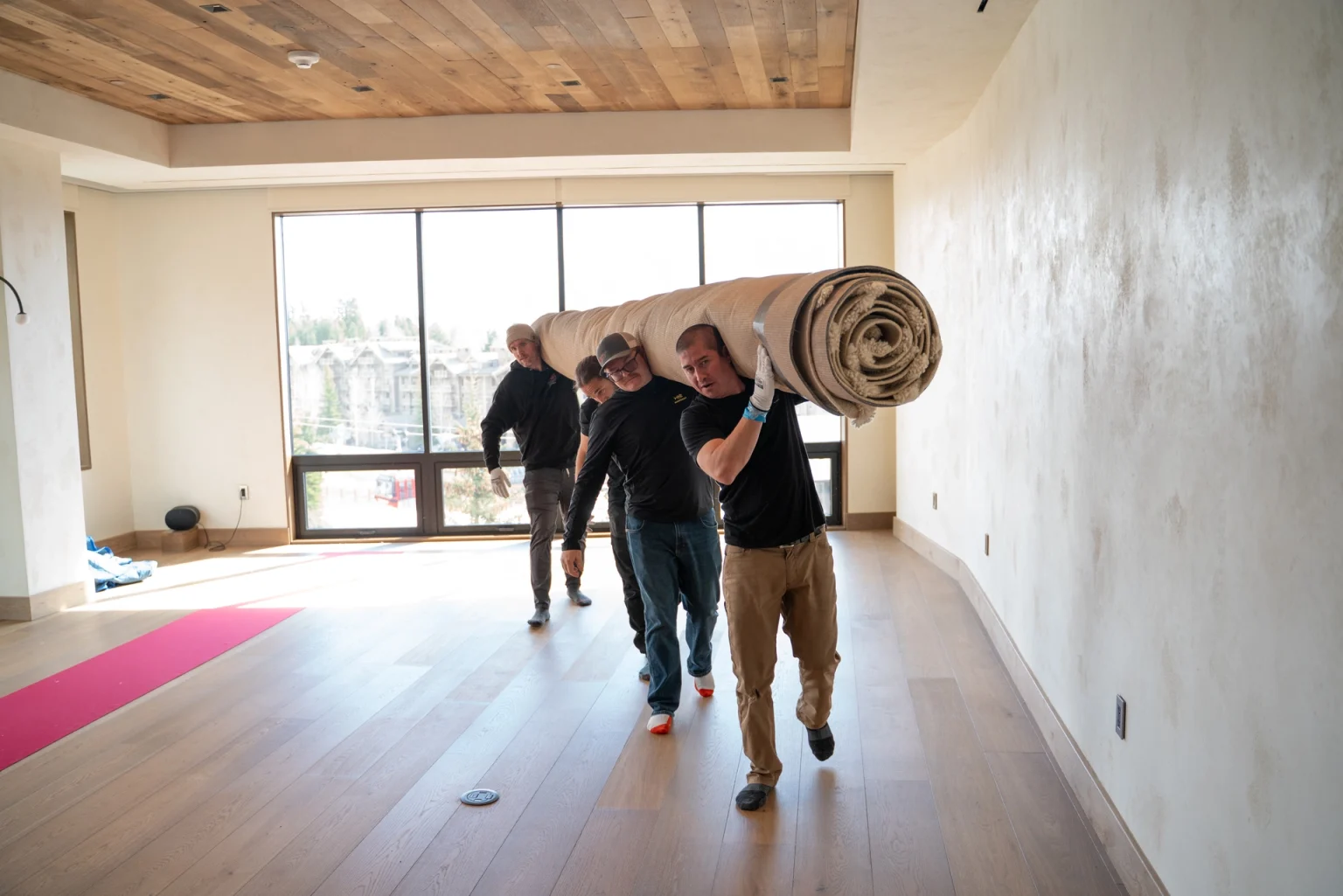 Four We Lift Things crew members carry a large rolled rug together on their shoulders through an empty Jackson Hole home.